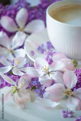 Delicate spring flowers of lilac and jasmine and a cup of coffee with milk. Delicate morning coffee with a wonderful spring-summer mood. Soft selective artistic focus. 