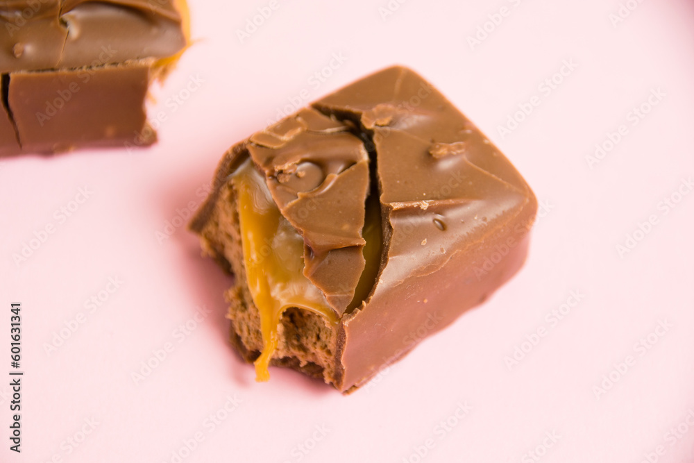 Pieces of a chocolate bar with caramel macro on a pink background Pieces of a chocolate bar with caramel macro on a pink background