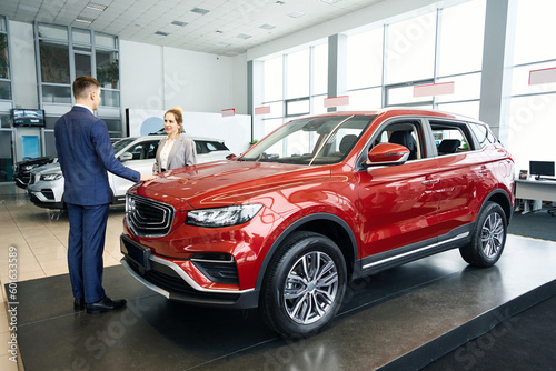 Happy man and woman in suits standing near red car