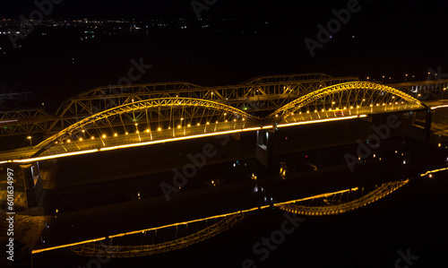 Bright lights, bridges with arches, night city. A road bridge across the river, taken from a drone.
