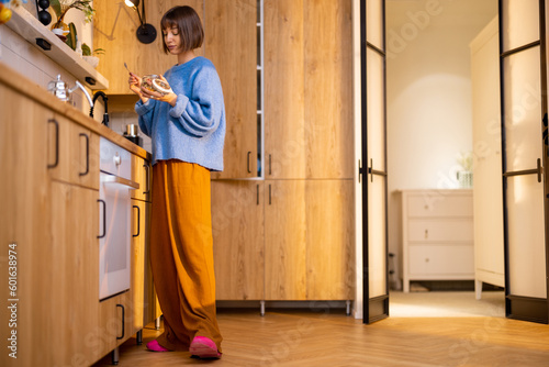 Young woman gets some breakfast on kitchen of modern studio apartment. Domestic lifestyle and interior concept