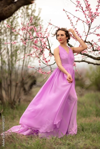 Woman peach blossom. Happy curly woman in pink dress walking in the garden of blossoming peach trees in spring