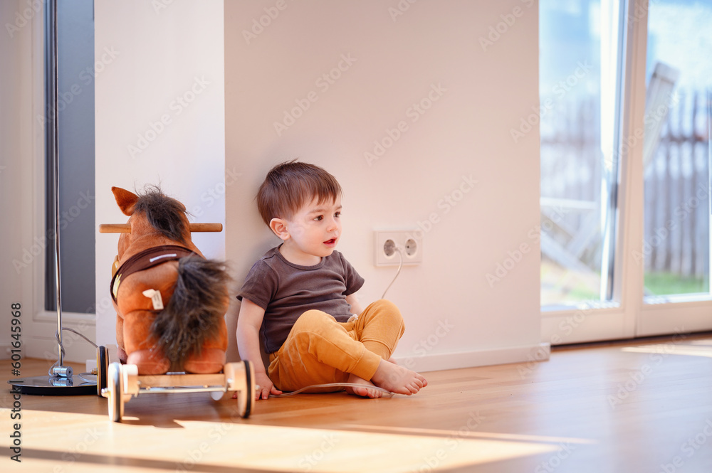 Little toddler boy playing with electricity wire in light white home. Little toy horse near Little toddler boy playing with electricity wire in light white home. Little toy horse near