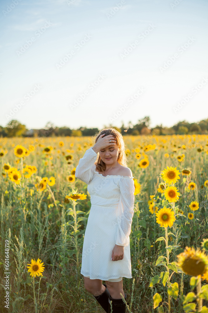 Young beautiful blonde woman in white dress in field of sunflowers at sunset. Evening sun rays. Summer. Young beautiful blonde woman in white dress in field of sunflowers at sunset. Evening sun rays. Summer.