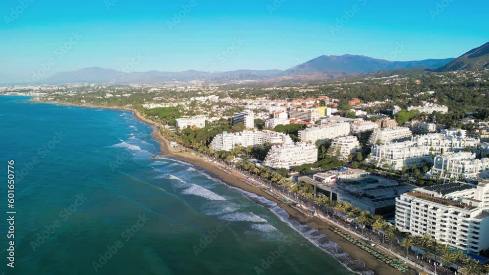 Drone clip over shoreline in Marbella showing open clear blue sea, sandy beach and tall hotel buildings Drone clip over shoreline in Marbella showing open clear blue sea, sandy beach and tall hotel buildings