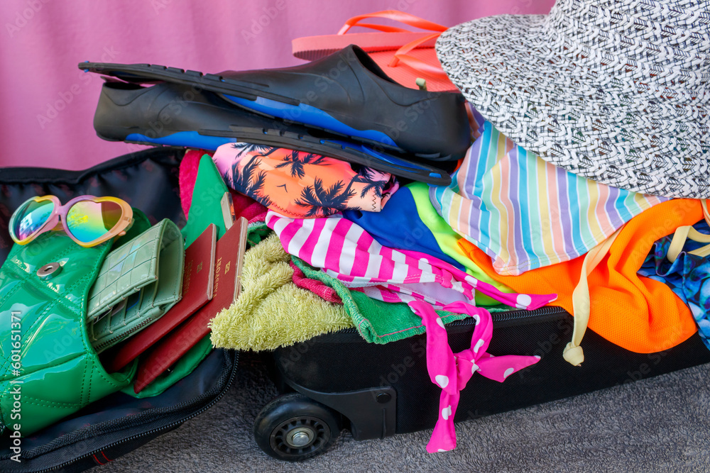 Open suitcase with clothes, swimsuits and other summer vacation items