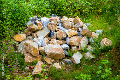 A mountain of rocks on the grass and in the bushes.