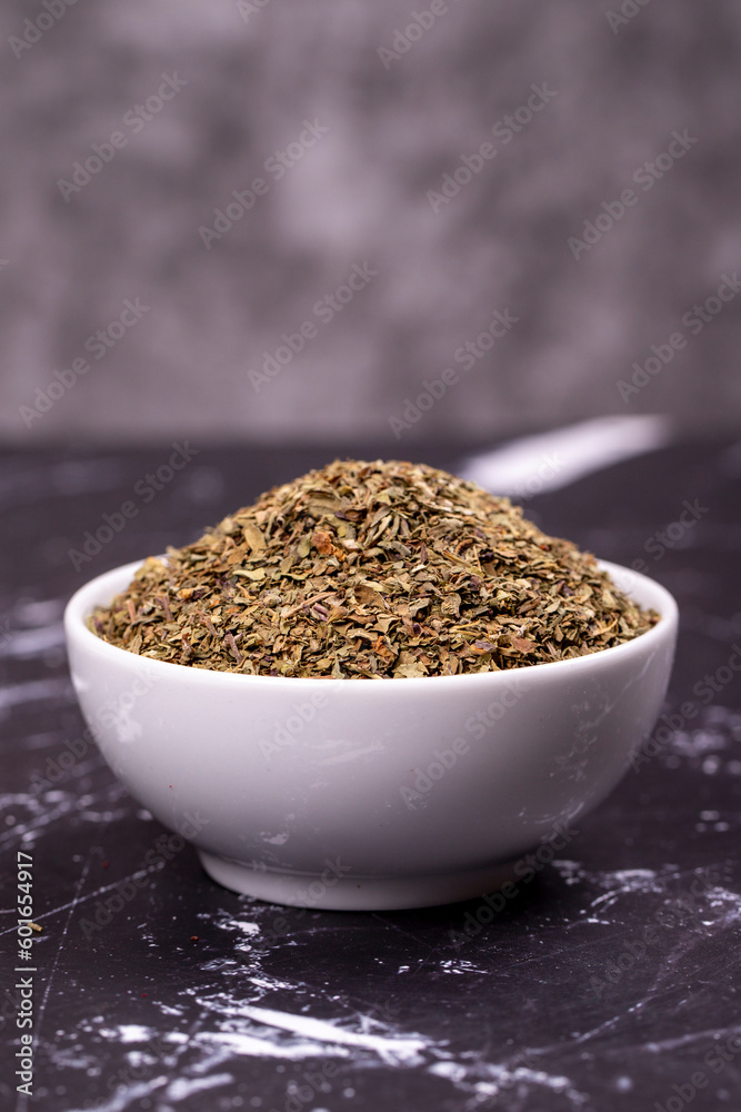 Dried crushed basil on dark background. Dried ground basil powder spices in ceramic bowl. Spice concept. Close up