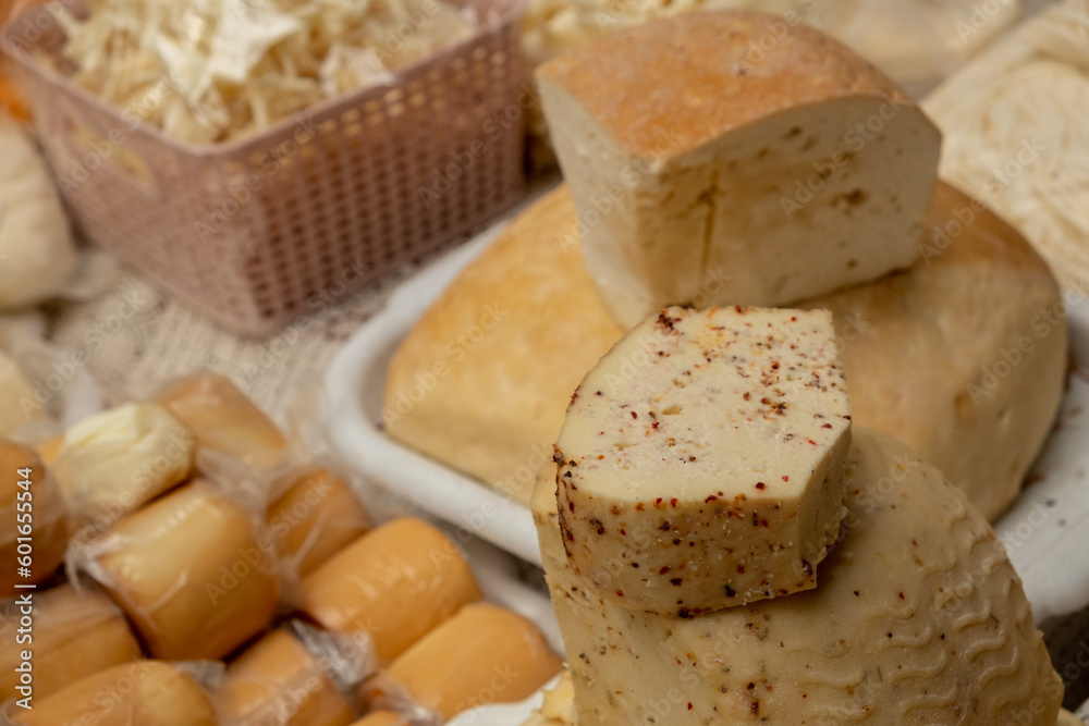 Wheels of rustic cheese with spices on the counter against the backdrop of a large assortment of cheeses at the Ukrainian food market.