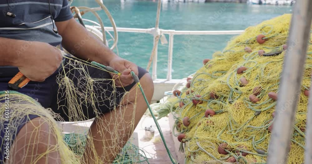 A local fisherman fixes holes and tangles in his fishing net, slow motion