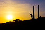 Man saluting the sun in silhouette of factory chimneys.
