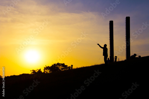 Man saluting the sun in silhouette of factory chimneys.