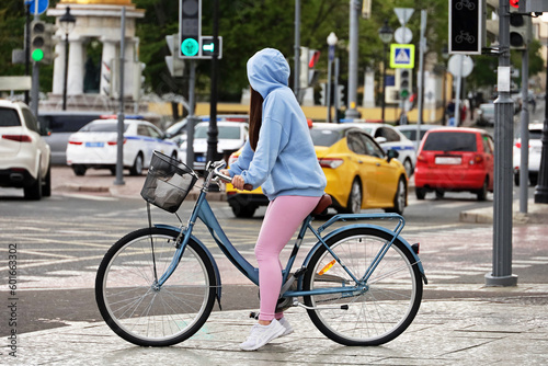 Girl stopped with bicycle on a street on cars background. Cycling in spring city
