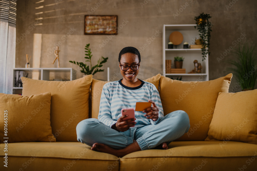 African american woman using credit card and asmartphone while online shopping at home African american woman using credit card and asmartphone while online shopping at home