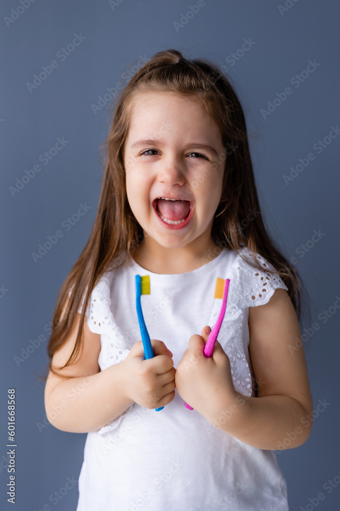 a little brunette girl holds a toothbrush in her hands on a plain gray background, space for text. Pediatric dentistry a little brunette girl holds a toothbrush in her hands on a plain gray background, space for text. Pediatric dentistry