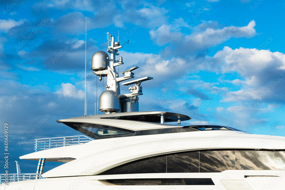 Luxurious large motor white yacht with satellite dishes on the roof against the blue sky with clouds, close-up.