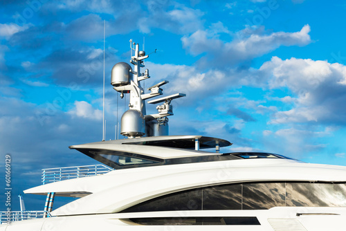 Luxurious large motor white yacht with satellite dishes on the roof against the blue sky with clouds, close-up. © Сергей Жмурчак