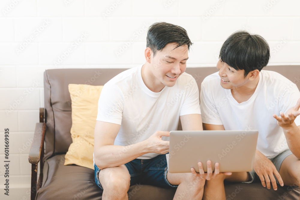 Asian Gay Couple Using Computer For Video Conference On Sofa. Cheerful young gay couple smiling cheerfully while shopping online at home.