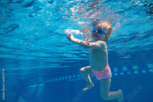 Cute, smiling, happy little baby girl, toddler in swimsuit and goggles swimming underwater in swimming pool. Enjoyment. Concept of sport, healthy and active lifestyle, childhood, fun and training