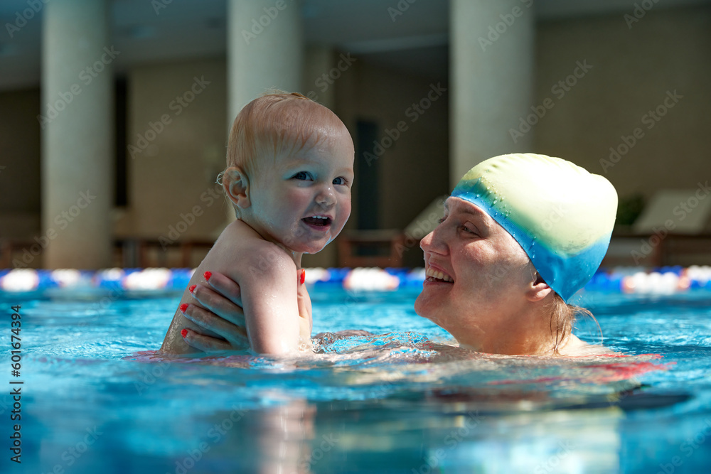 Happy mother, smiling, holding cute with little kid, girl, daughter in swimming pool indoors on warm sunny day. Concept of sport, healthy and active lifestyle, childhood, fun and training