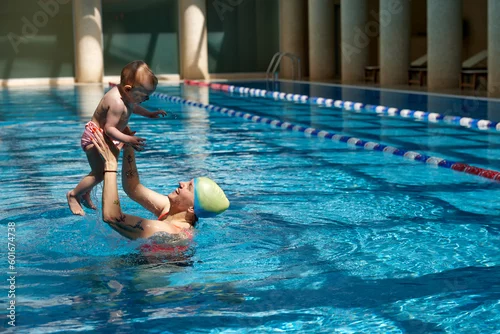 Obraz Happy mother with little kid, girl, daughter in swimming pool indoors on warm sunny day. Enjoying. Family time. Concept of sport, healthy and active lifestyle, childhood, fun and training