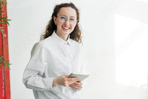 Using a tablet online surfing work daily woman with glasses in a white shirt curly redhead in the office, smiling looking away .