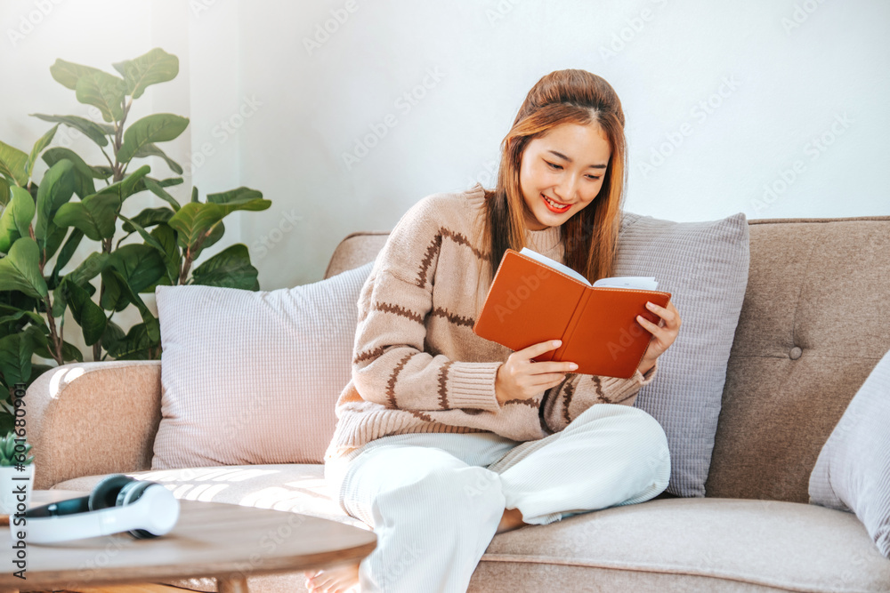 Pensive relaxed Asian woman reading a book at home relax and drinking coffee on sofa. Pensive relaxed Asian woman reading a book at home relax and drinking coffee on sofa.