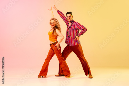 Fototapeta Naklejka Na Ścianę i Meble -  Artistic, expressive man and woman in stylish clothes dancing disco, retro dance against gradient pink yellow background. Concept of retro style, dance, fashion, art, hobby, music, 70s, hobby