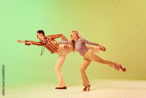 Stylish, expressive, talented young man and woman in vintage clothes dancing against gradient green yellow background. Concept of retro style, disco dance, fashion, art, hobby, music, 70s