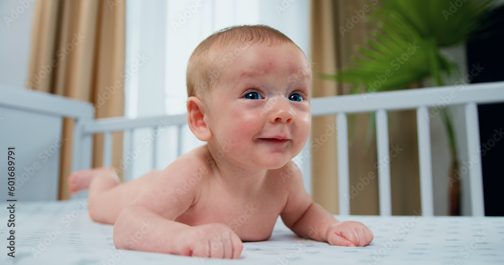 Cute and happy newborn baby boy is lying in white crib on his stomach