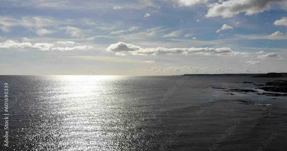 Aerial rising shot of the coastline with the sun glistening of the sea filmed in South Devon England Aerial rising shot of the coastline with the sun glistening of the sea filmed in South Devon England