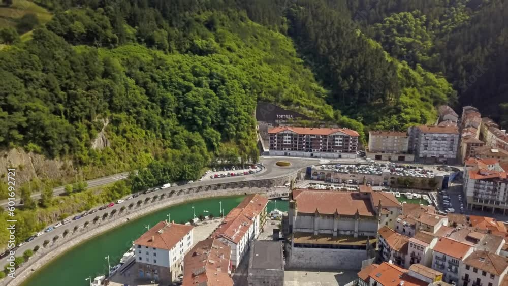 Aerial reverse dolly above ondarroa coastal port town canal and lush green mountainside