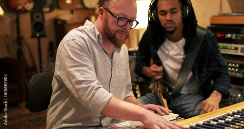 Young African American guitarist and music producer working on a track together during a session in a recording studio