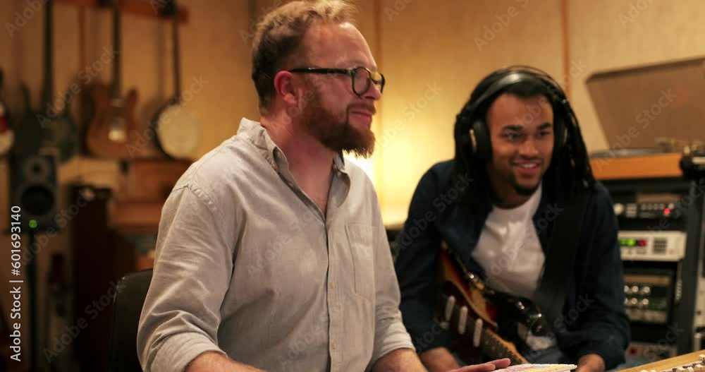 Young African American guitarist and music producer working on a track together during a session in a recording studio Young African American guitarist and music producer working on a track together during a session in a recording studio