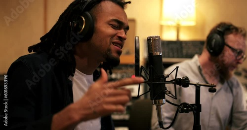 Young African American musician singing passionately into a microphone while laying down tracks in a recording studio