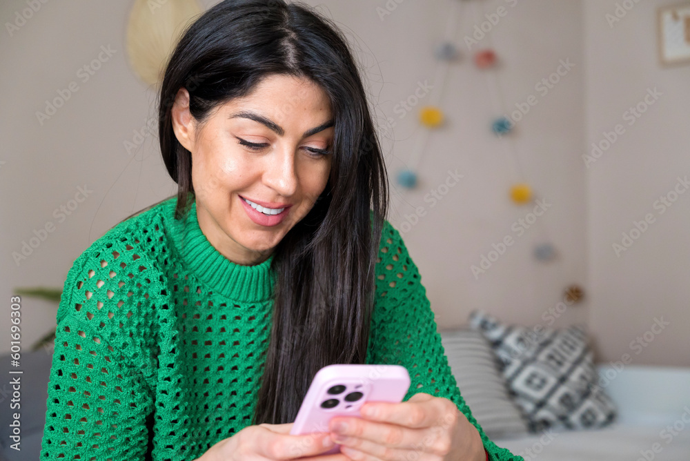 Beautiful young smiling woman sitting at home and using mobile phone Beautiful young smiling woman sitting at home and using mobile phone