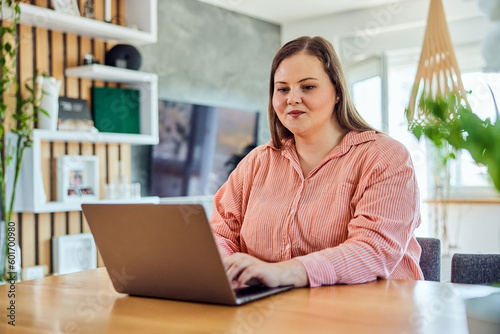 A pretty plus-size woman typing on a laptop keyword and working from home.