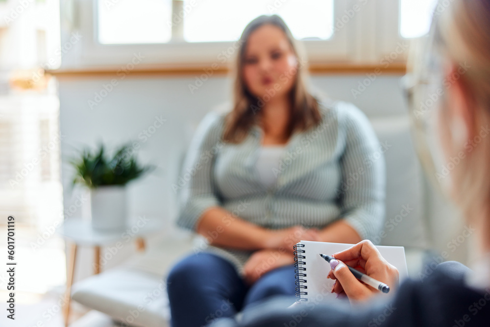 A female psychotherapist taking notes during a conversation with an overweight woman. - obrazy, fototapety, plakaty 