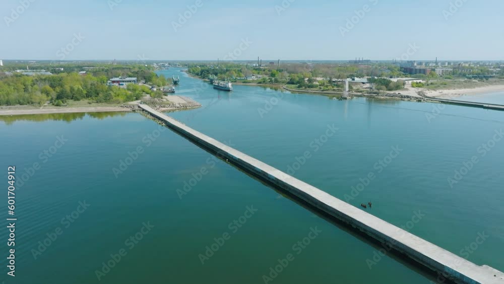 Aerial establishing view of large gray cargo ship entering Port of Liepaja (Latvia), Karosta bridge, sunny spring day, calm Baltic sea, city in background, distant wide drone dolly shot moving right Aerial establishing view of large gray cargo ship entering Port of Liepaja (Latvia), Karosta bridge, sunny spring day, calm Baltic sea, city in background, distant wide drone dolly shot moving right