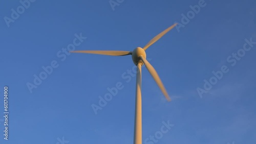 Beautiful view of wind turbine generating renewable energy in the wind farm, green countryside landscape, vibrant sunny spring evening with golden hour light, distant medium shot photo