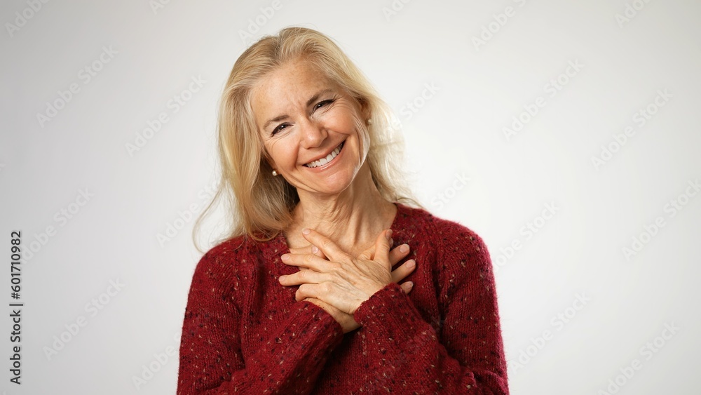 Mature woman, receives beautiful compliments, finally raises her hands puts hands on chest. Beautiful mature blond isolated on solid white background. Copy space Mature woman, receives beautiful compliments, finally raises her hands puts hands on chest. Beautiful mature blond isolated on solid white background. Copy space