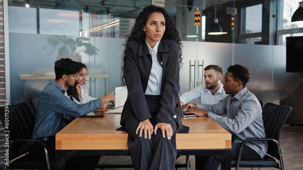 Worried sad upset leader woman worker businesswoman sitting on table in conference room thinking about business problem multicultural team colleagues in background discussing work project teamwork Worried sad upset leader woman worker businesswoman sitting on table in conference room thinking about business problem multicultural team colleagues in background discussing work project teamwork