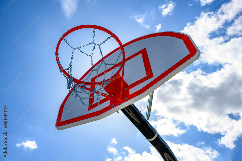 A new basketball backboard with a new hoop and metal netting has a beautiful blue sky with white puffy clouds in the background. Looking up at basketball net outdoors in Windsor in Upstate NY. A new basketball backboard with a new hoop and metal netting has a beautiful blue sky with white puffy clouds in the background. Looking up at basketball net outdoors in Windsor in Upstate NY.