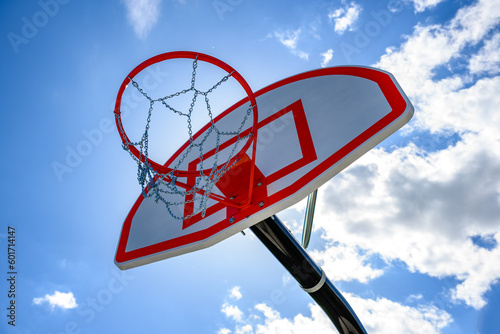 A new basketball backboard with a new hoop and metal netting has a beautiful blue sky with white puffy clouds in the background.  Looking up at basketball net outdoors in Windsor in Upstate NY. © Chet Wiker