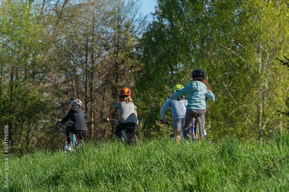 Group of children riding bicycles in nature on a lush green hillside, spring season city, bicycle helmets on the head of cyclists, spring sunny weather, children travel, authentic healthy lifestyle