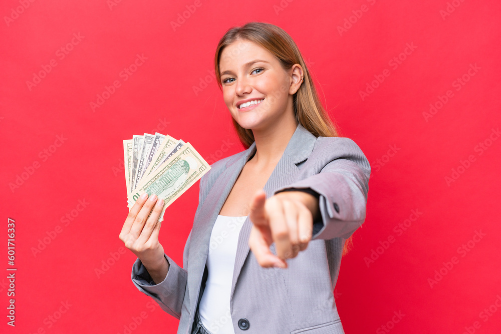 Young business caucasian woman holding money isolated on red background pointing front with happy expression Young business caucasian woman holding money isolated on red background pointing front with happy expression