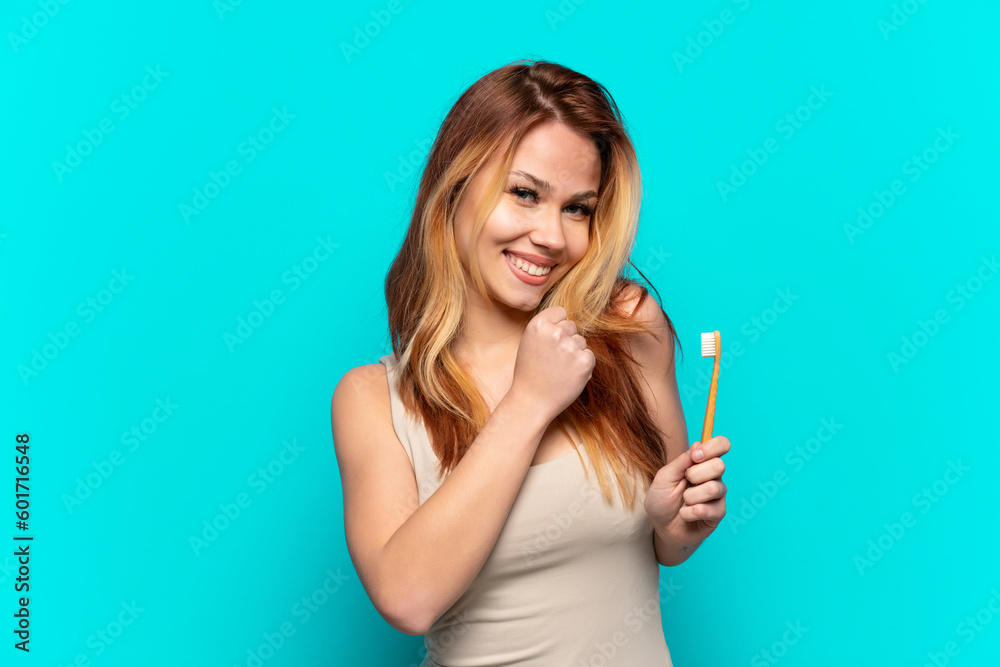 Teenager girl brushing teeth over isolated blue background celebrating a victory Teenager girl brushing teeth over isolated blue background celebrating a victory