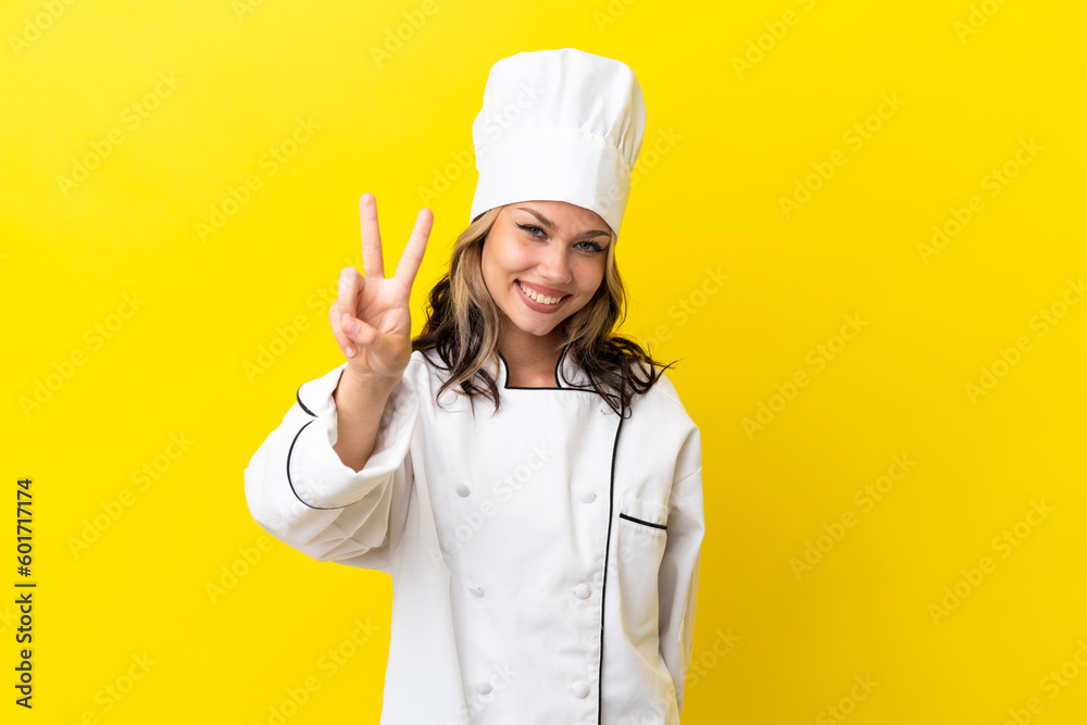 Young Russian chef girl isolated on yellow background smiling and showing victory sign Young Russian chef girl isolated on yellow background smiling and showing victory sign