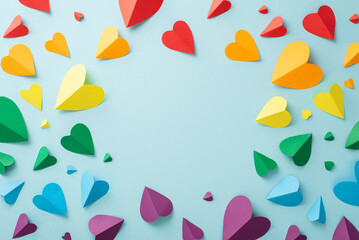 Top-down view of parade essentials for LGBT History Month. A lot of colorful paper hearts, arranged on a pastel blue background with a blank frame for text or advertisements
