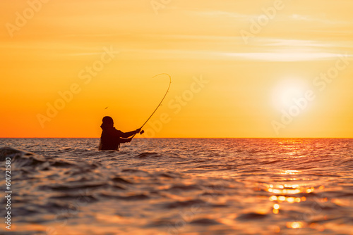 Silhouette eines Angler in wasserdichten Hosen welcher vor einem traumhaften orangen Sonnenuntergang in der Ostsee angelt / fischt . Er steht mitten im Wasser der Ostsee.